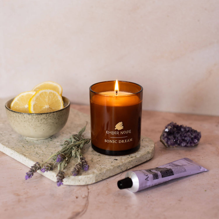 Candle with flame on marble tile with lavender, crystals and bergamot
