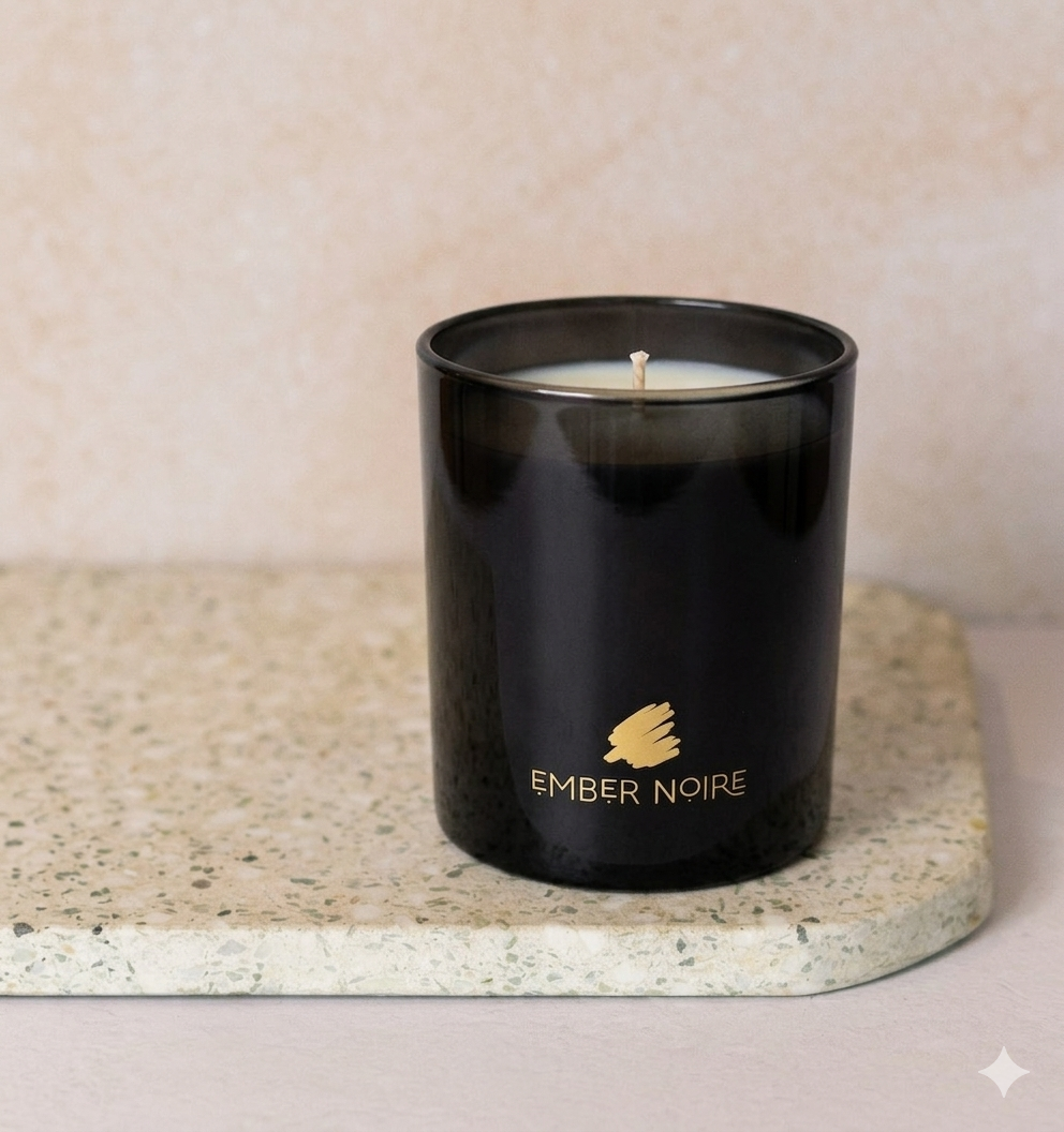 Black candle in a container with 'Ember Noire' branding on a beige surface.