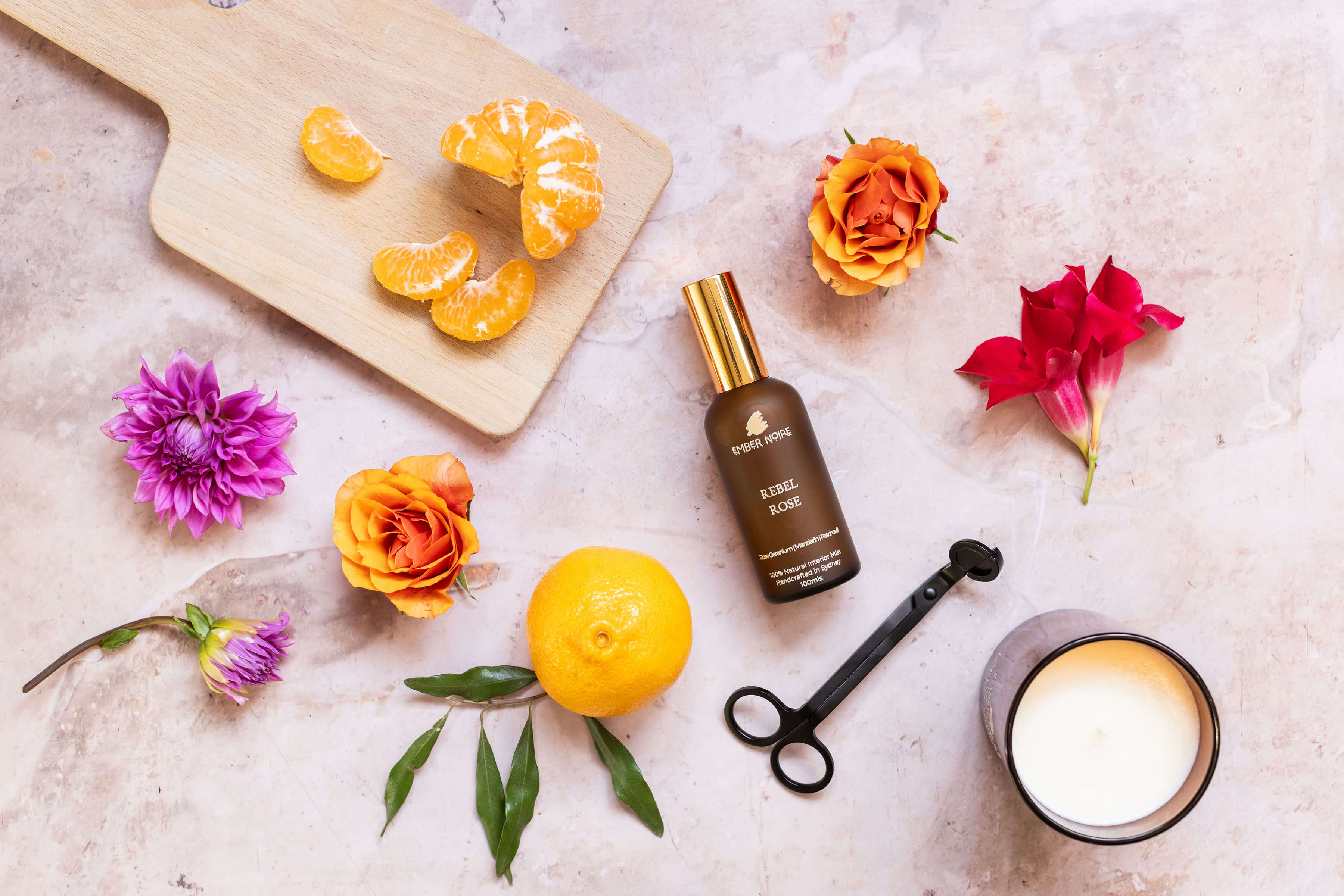 Cosmetic bottle with flowers, fruits, and a candle on a textured surface